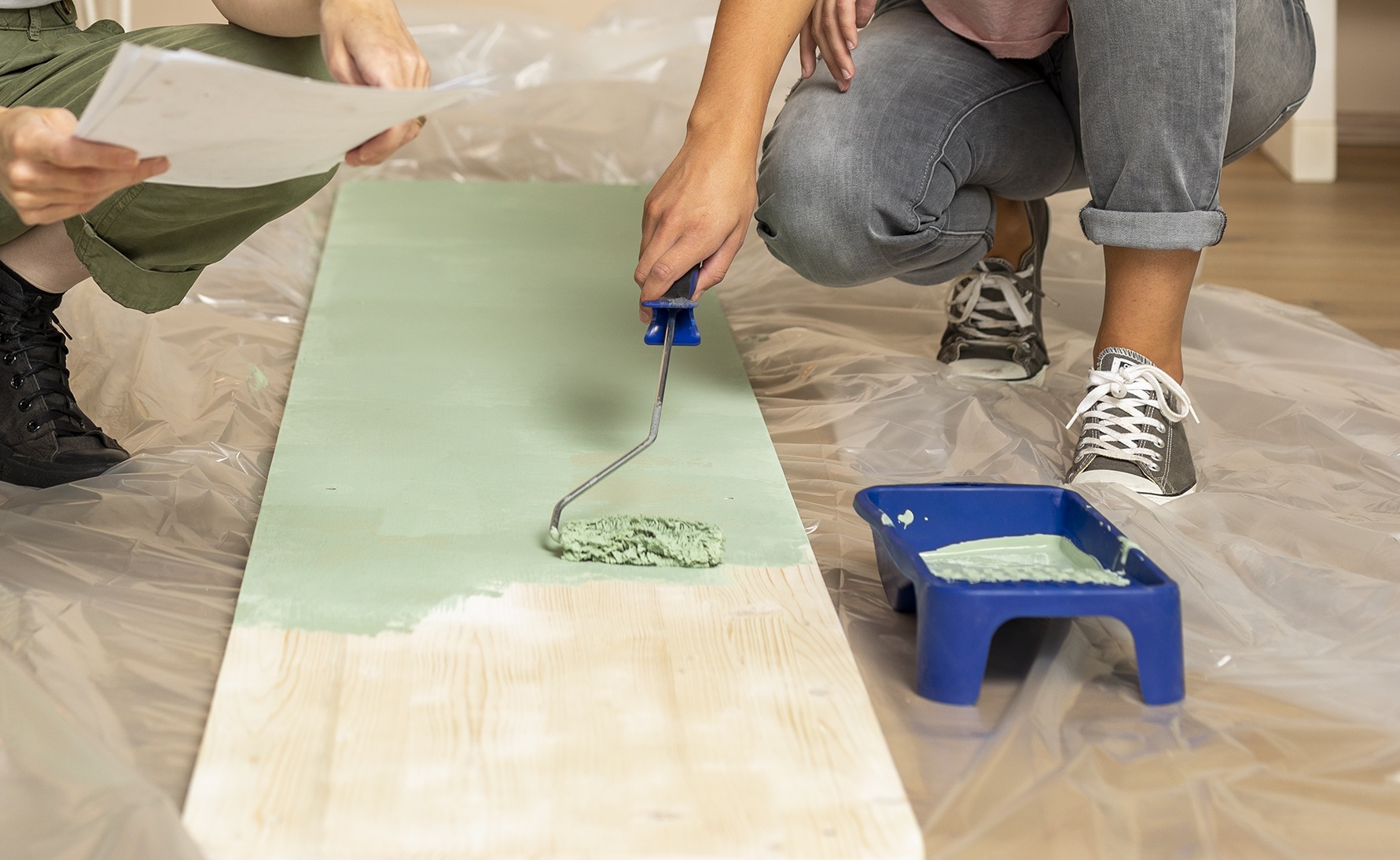 Zwei Menschen streichen ein Holzteil in grün.