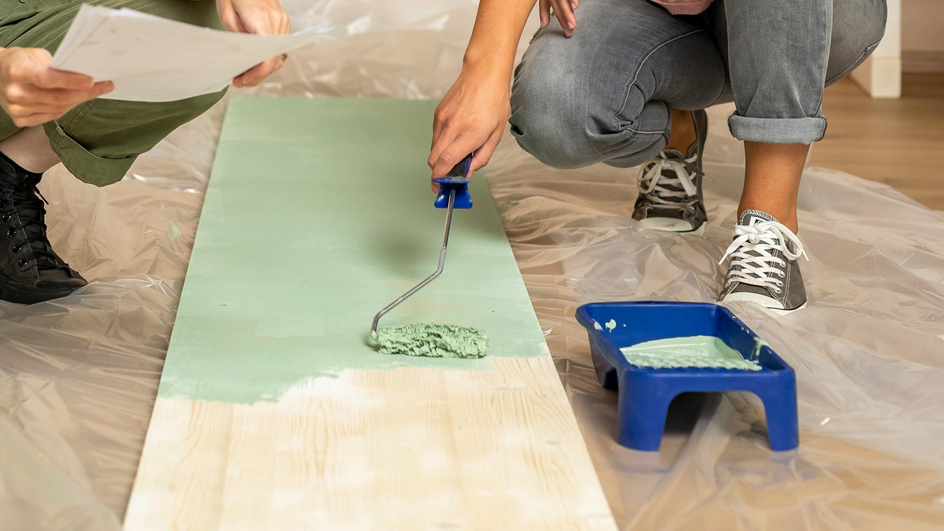 Zwei Menschen streichen ein Holzteil in grün.