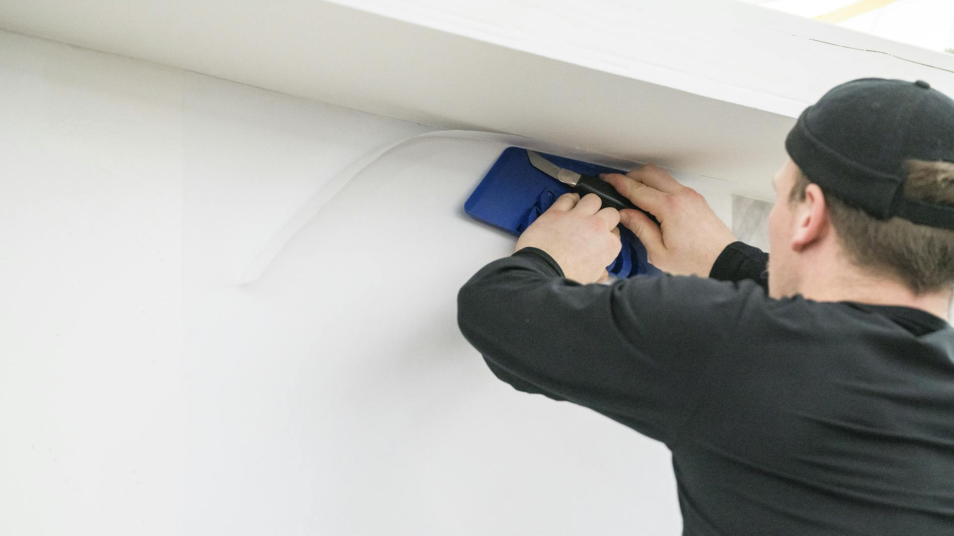 Heimwerker schneidet überstehende Tapete an Ecke zwischen Wand und Decke mit Cutter ab.