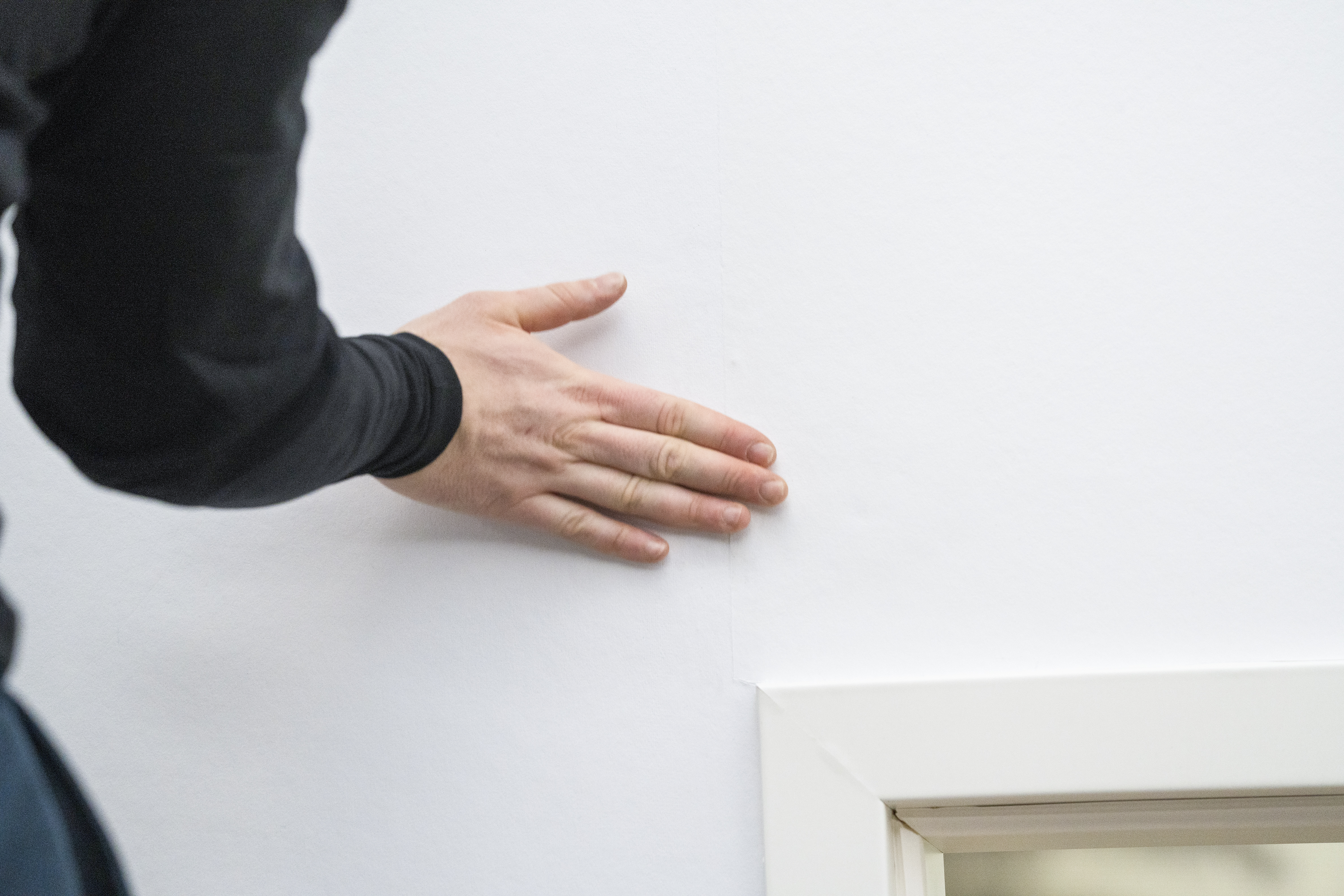 Jemand tapeziert Renoviervlies am Türrahmen.