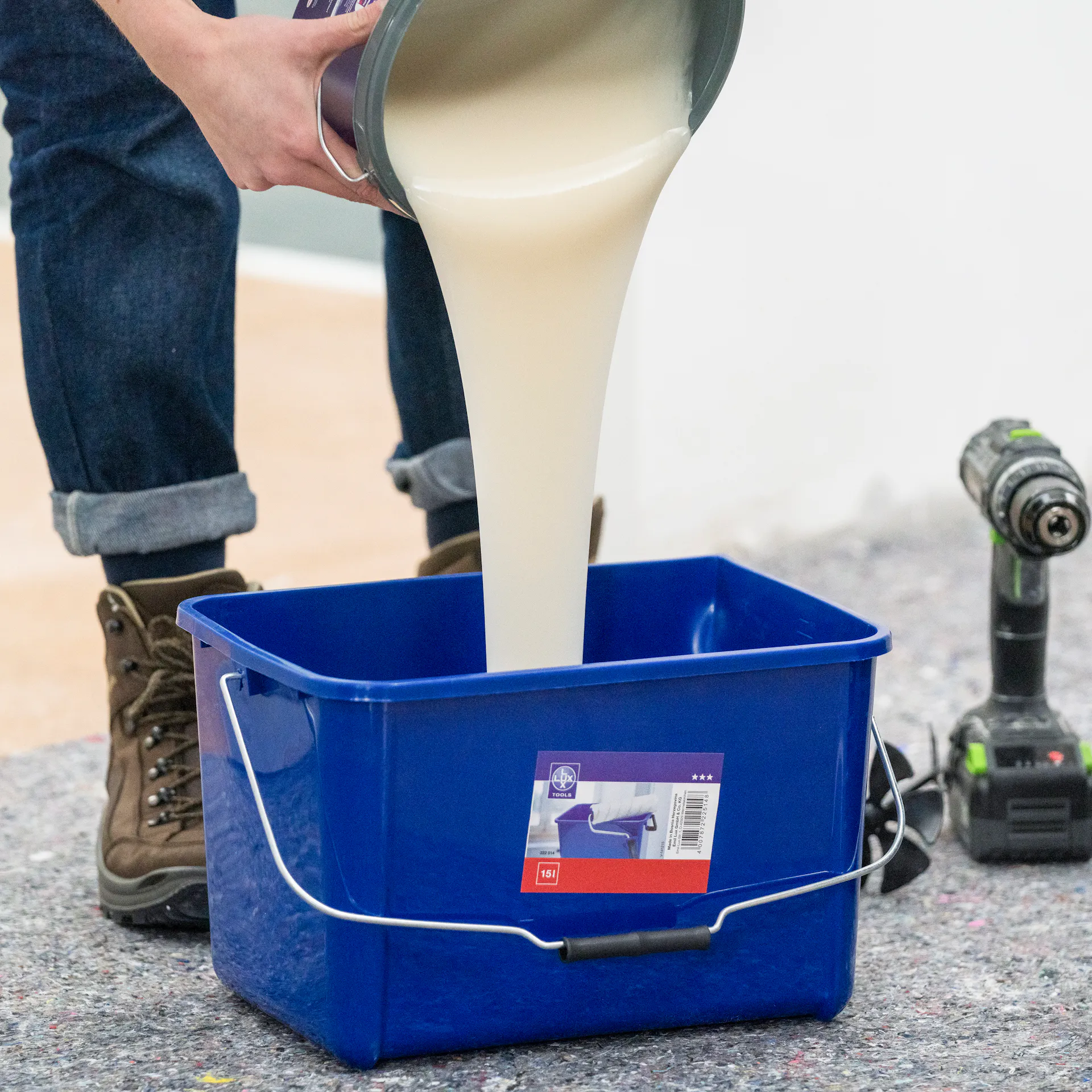 Někdo nalévá lepidlo do modrého kbelíku, podlaha je zakrytá netkanou textilií.