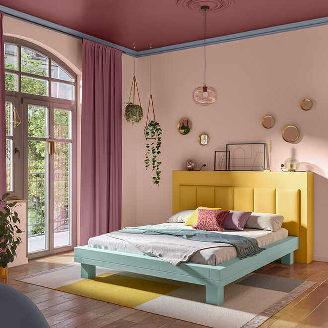 Bett Ludwig, wo eine schmale gelbe Konsole am Kopfende liegt, steht in einem farbenfrohen Raum, wessen Decke magenta rot gestrichen worden ist.