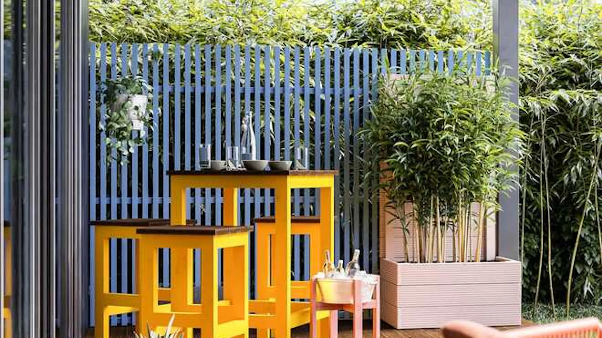 Sitzgruppe Ede für den Außenbereich steht links von Hochbeet Alfred vor einer blauen Sichtschutzwand auf einer Terrasse.