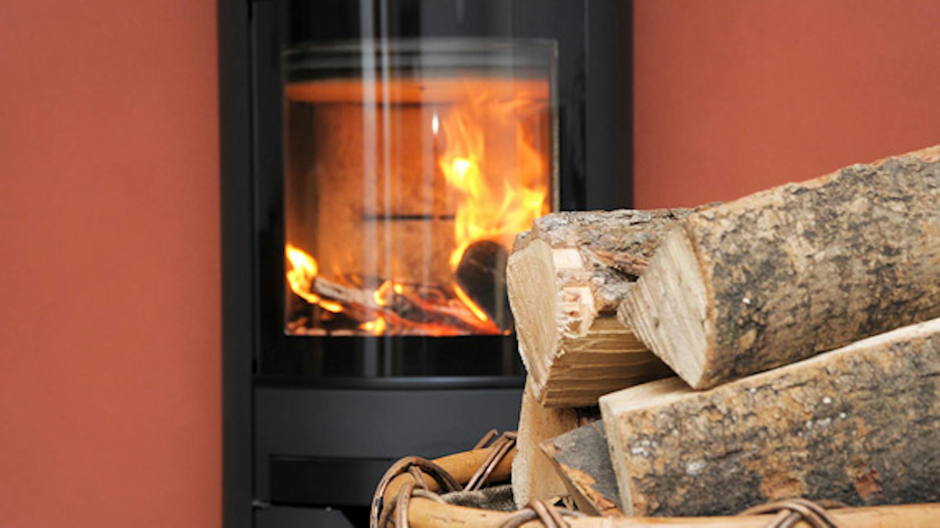 Holzscheite liegen in einem Korb vor einem brennenden Kamin