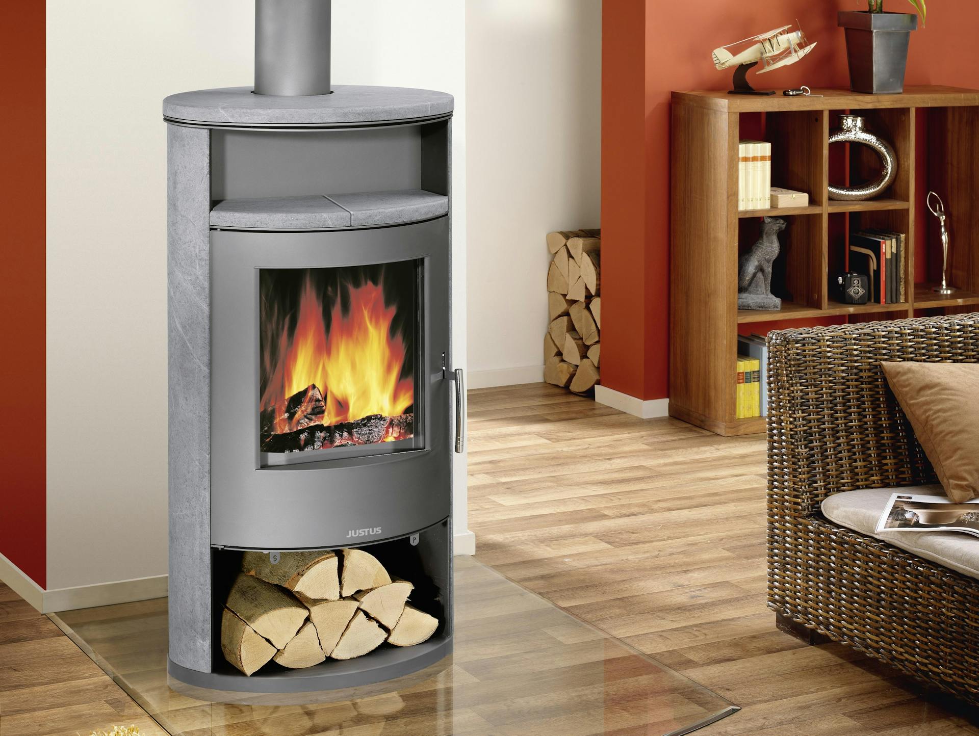 Ein wasserführender Kamin steht. Er ist mit dem Ofenrohr an eine weiße Wand angeschlossen und in Betrieb. Dieser steht in einem Wohnzimmer mit roten Wänden.