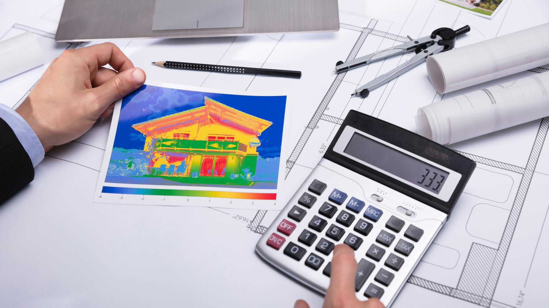 Ein Bauplan, ein Wärmebildfoto eines Hauses und ein Taschenrechner auf einem Schreibtisch.