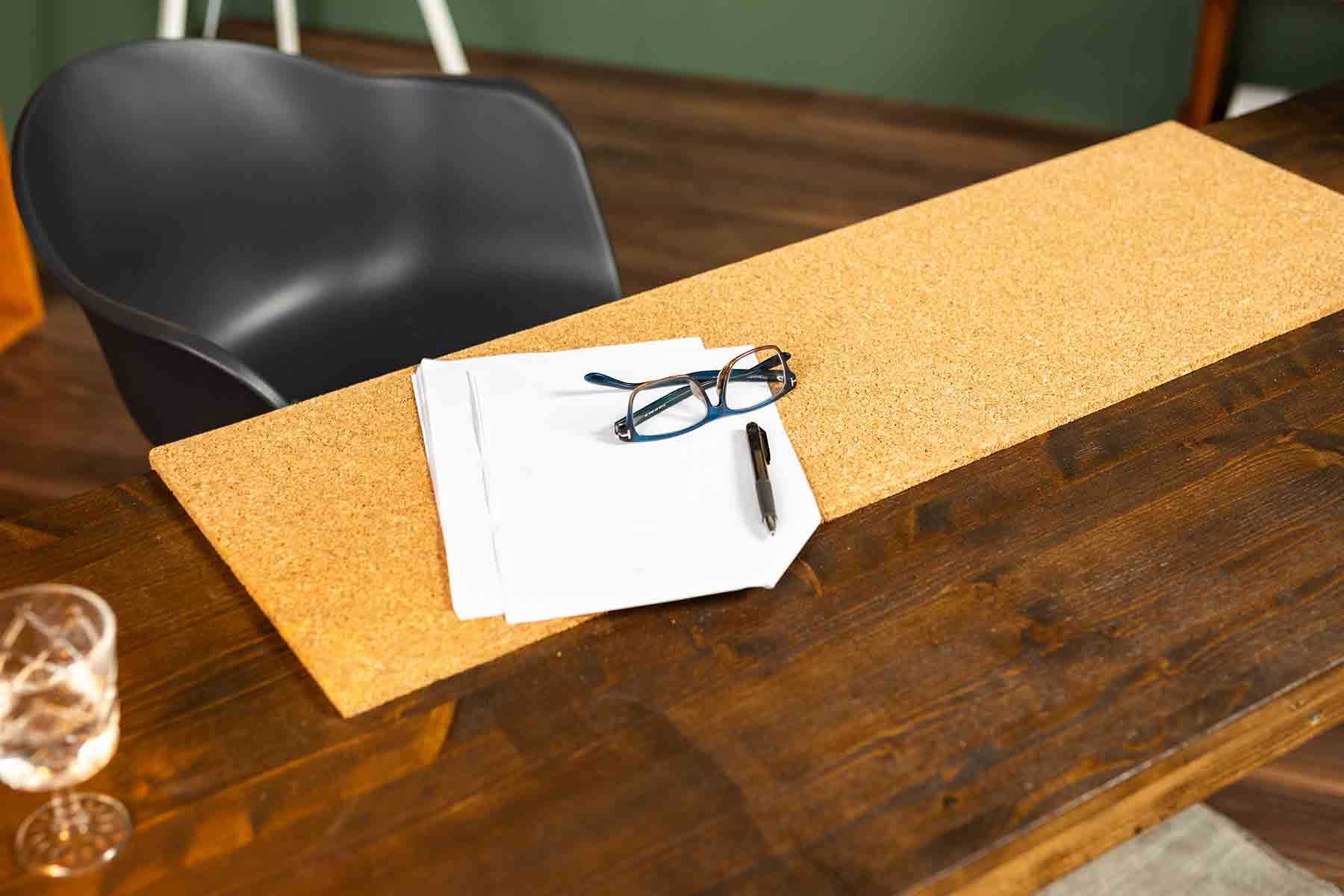 Auf Schreibtisch Egon in Dunkelbraun liegt eine Korkplatte, auf der Zettel und eine Brille abgelegt wurden