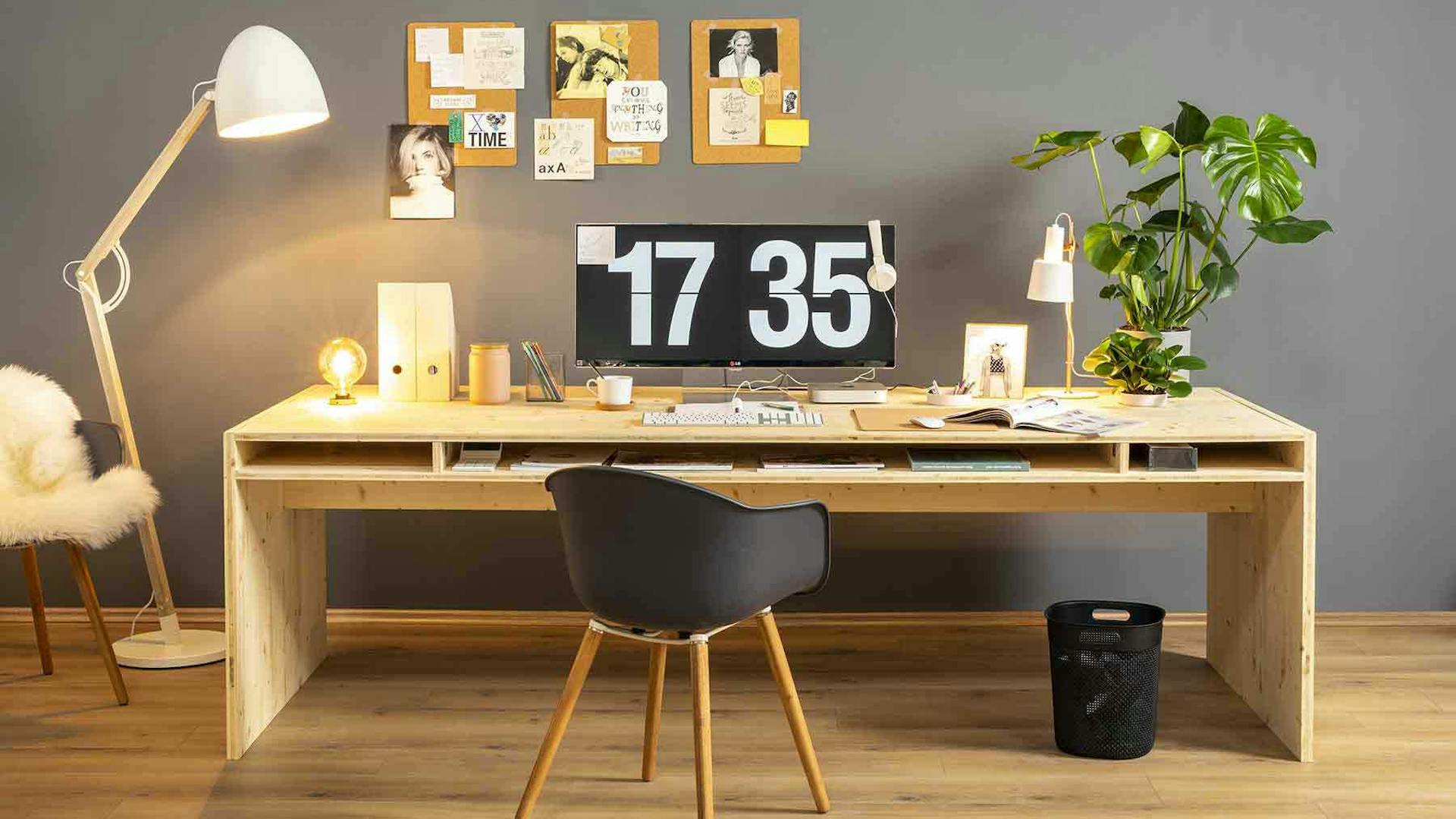 Frontansicht des aus Vollholz bestehenden Schreibtisch Otto in naturfarbe mit viel Arbeitsfläche vor einer grauen Wand.