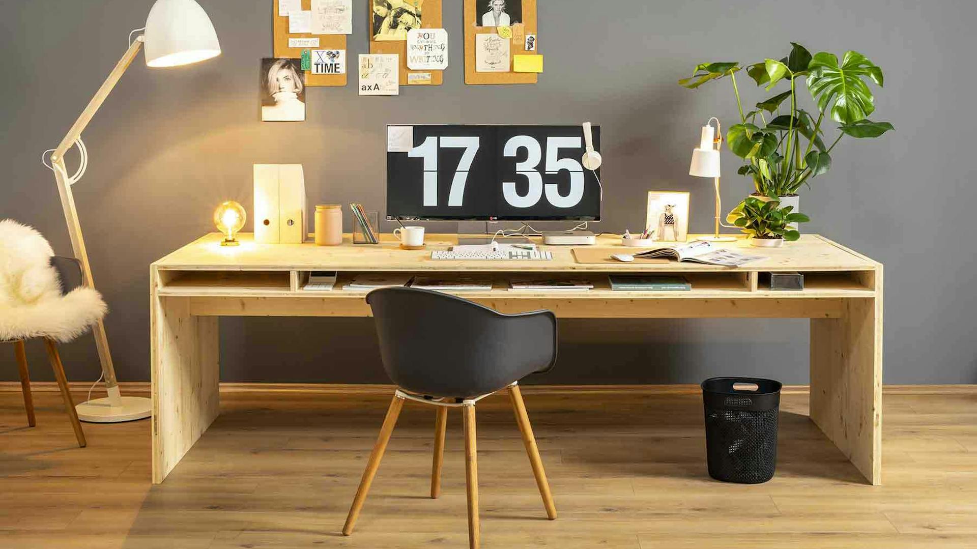 Frontansicht des aus Vollholz bestehenden Schreibtisch Otto in naturfarbe mit viel Arbeitsfläche vor einer grauen Wand.