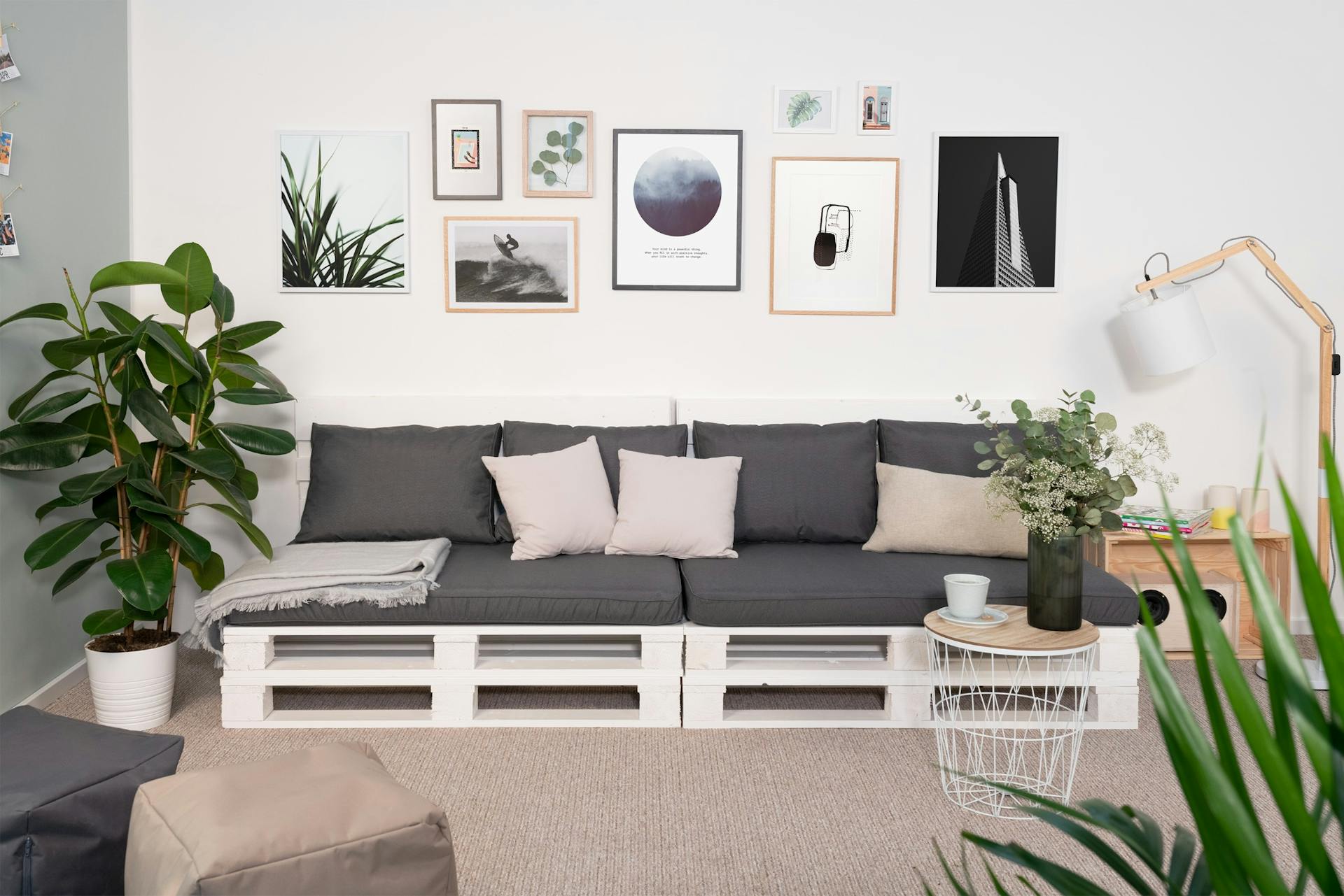 Weißes Palettensofa mit grauen Auflagen in Wohnzimmer auf Teppich vor Wand mit gerahmten Bildern