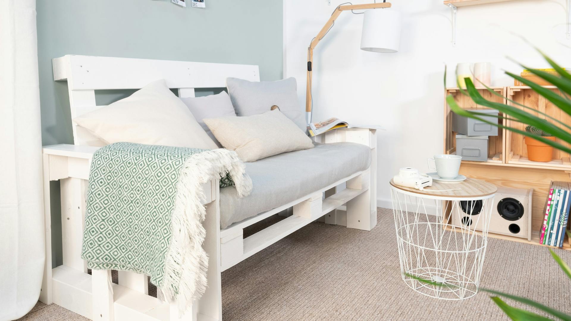 Divano di pallet con braccioli in soggiorno su tappeto davanti a una parete celeste