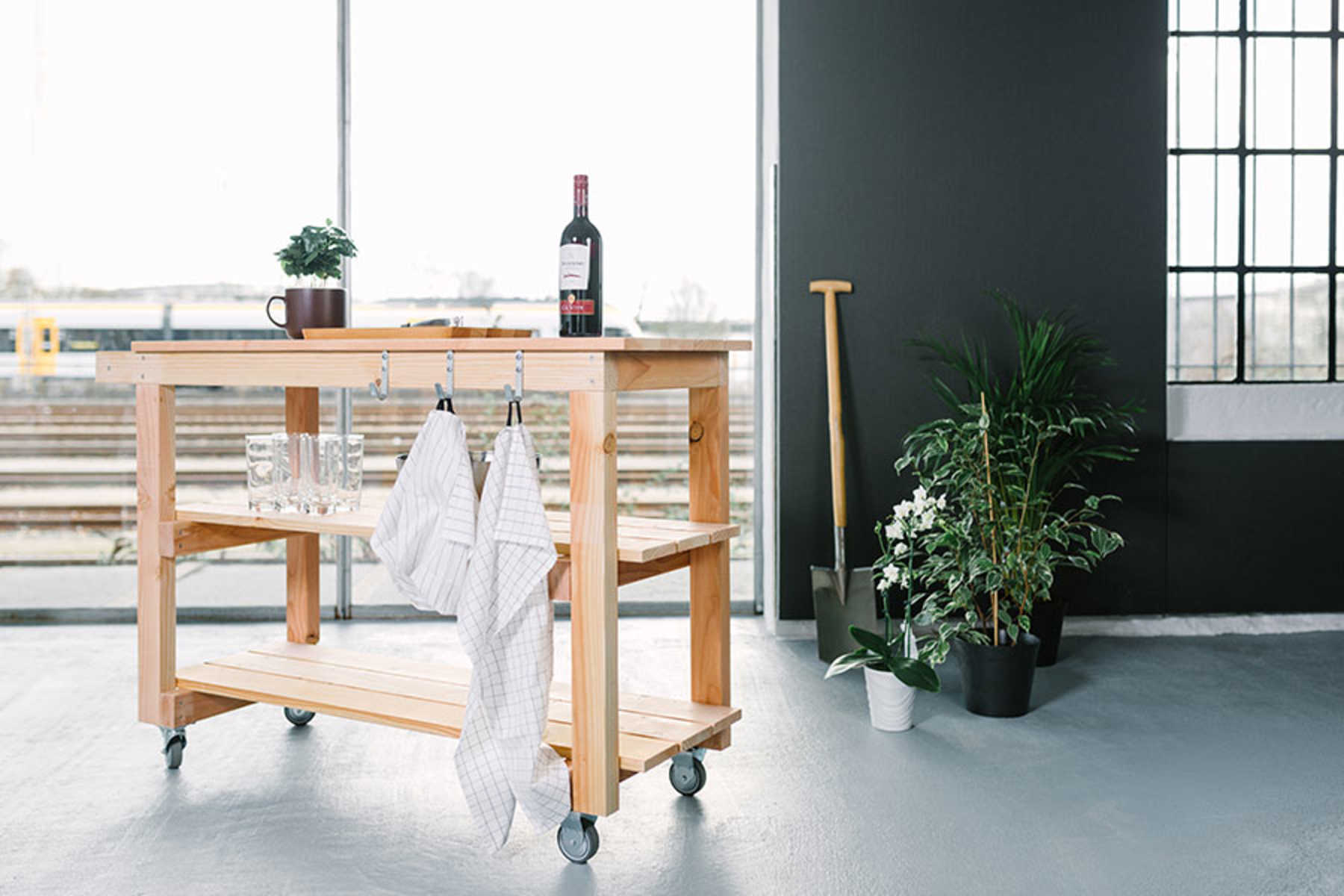 Auf Servierwagen Sophie ist Geschirr und Wein platziert. An den Haken des Wagens hängen Küchen-Handtücher.