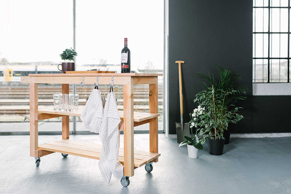 Auf Servierwagen Sophie ist Geschirr und Wein platziert. An den Haken des Wagens hängen Küchen-Handtücher.