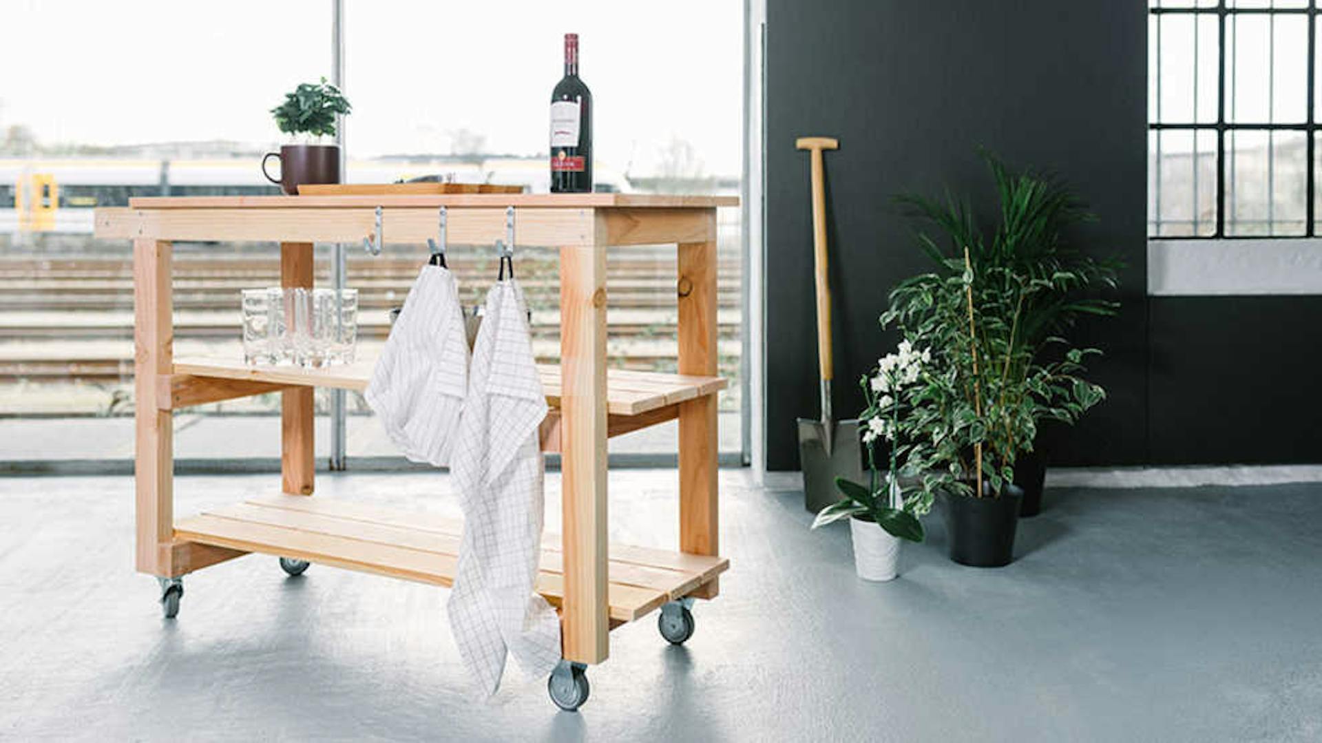 Auf Servierwagen Sophie ist Geschirr und Wein platziert. An den Haken des Wagens hängen Küchen-Handtücher.