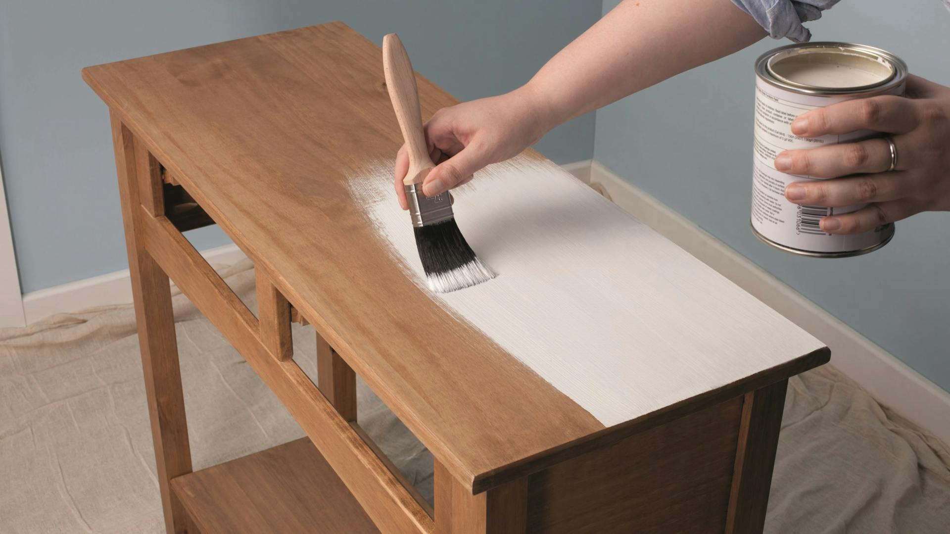 Mit einem Pinsel wird weiße Kreidefarbe für Shabby Chic auf ein altes Möbel aufgetragen