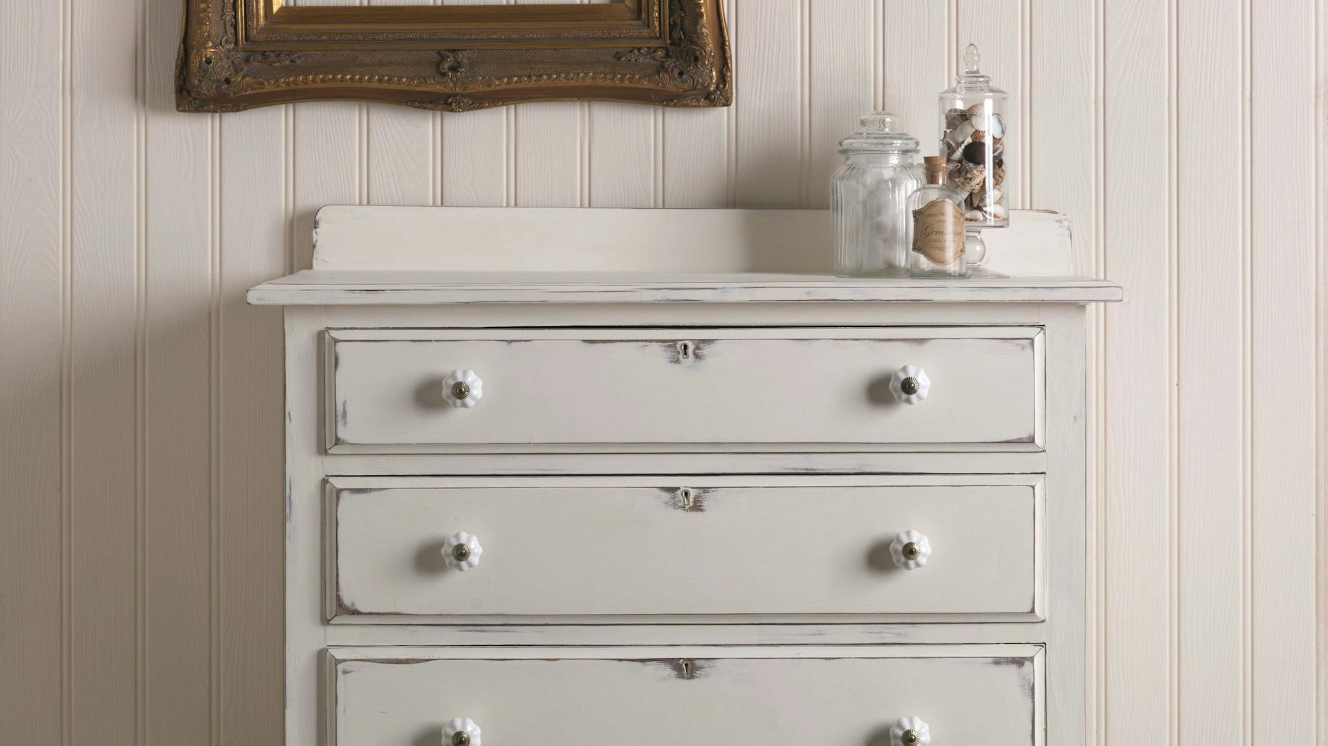 Selbstgemachte Shabby-Chic-Kommode mit weißer Kreidefarbe vor Wand mit Holzverkleidung