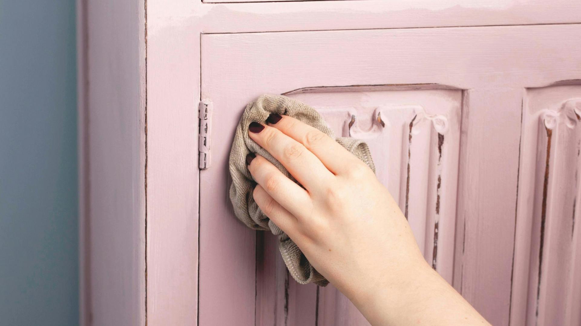 Mit einem Tuch wird Wachs auf ein rosa Holzmöbel im Shabby-Look aufgetragen