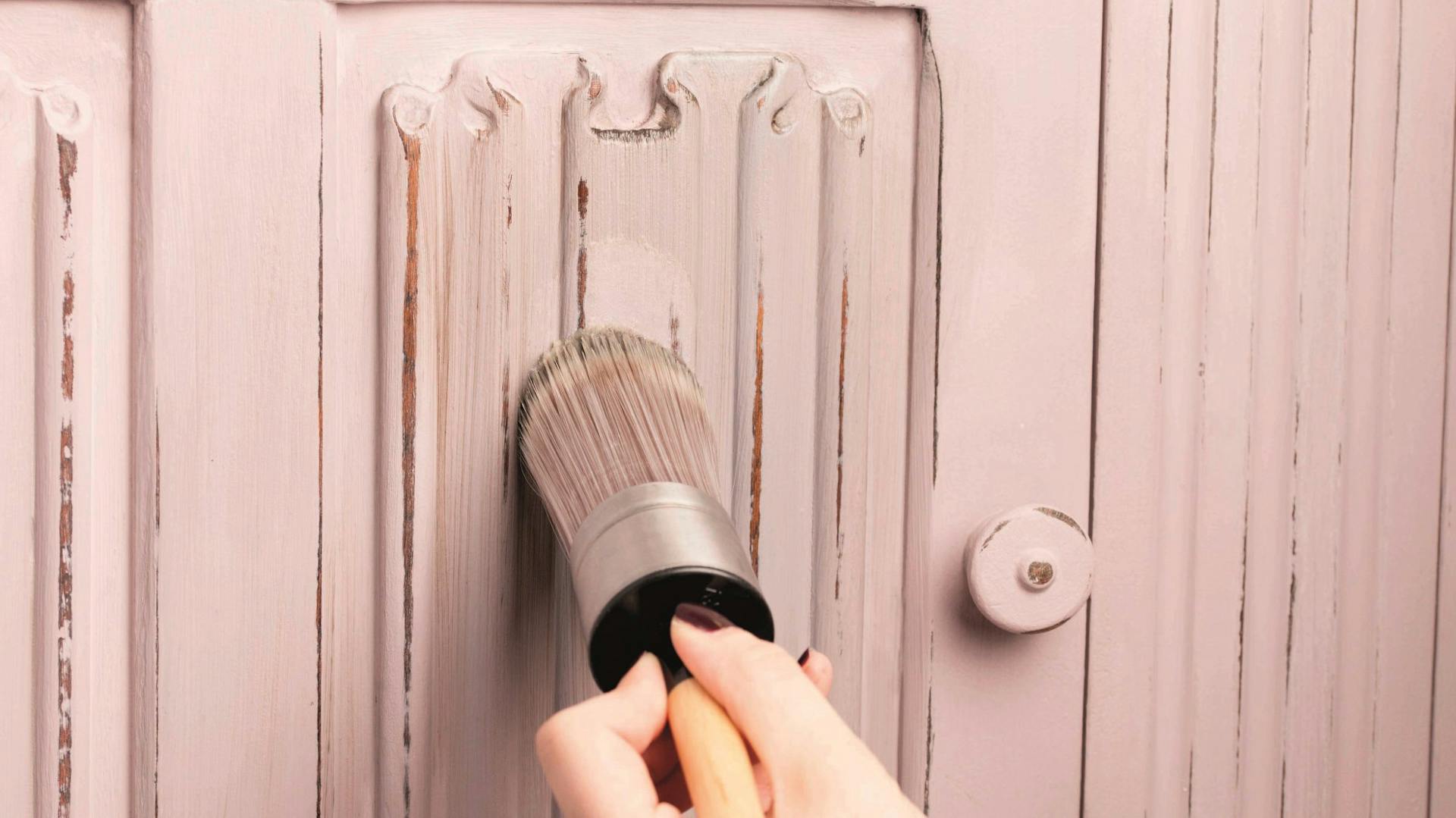 Mit einem Pinsel wird rosa Kreidefarbe für Shabby Chic auf eine Holztür aufgetragen