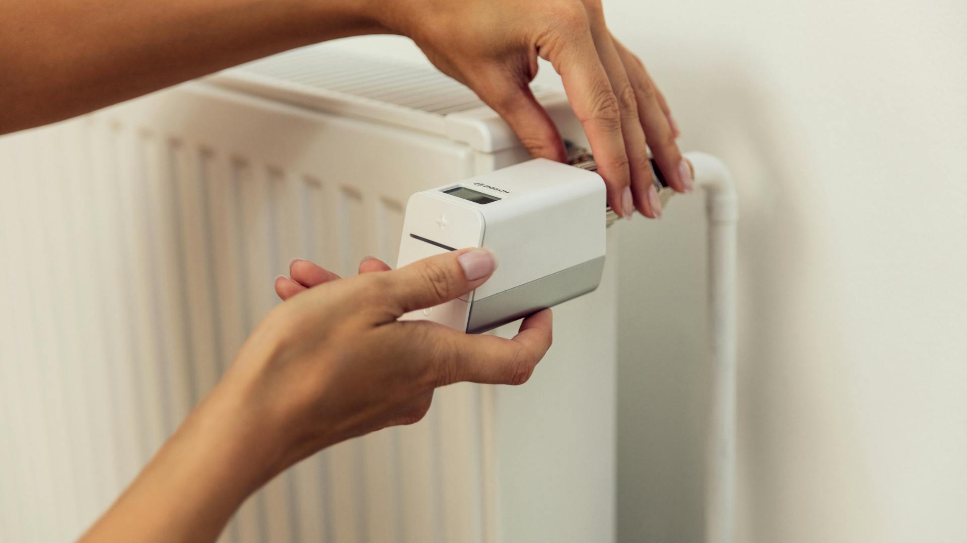 Egy személy felszereli egy radiátortermosztátot.