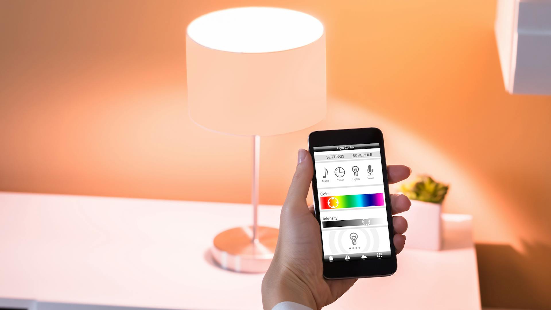 Person hält Smartphone zur Steuerung von Leuchten vor Tischlampe