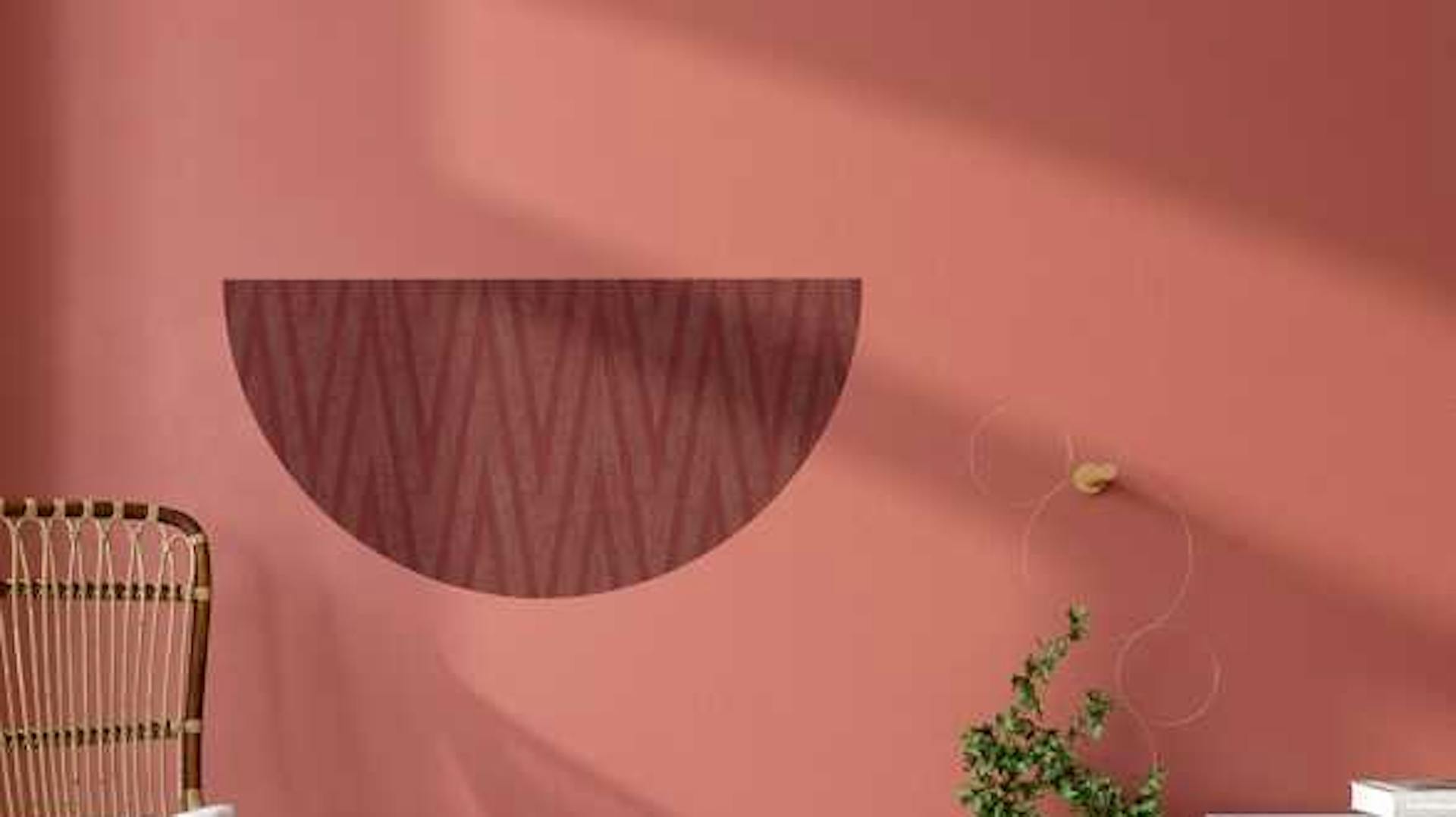 Ein Sessel aus Rattan und eine Rankhilfe aus Drahtringen stehen vor einer roten Wand, an der eine individuelle Form aus Tapete angebracht worden ist.