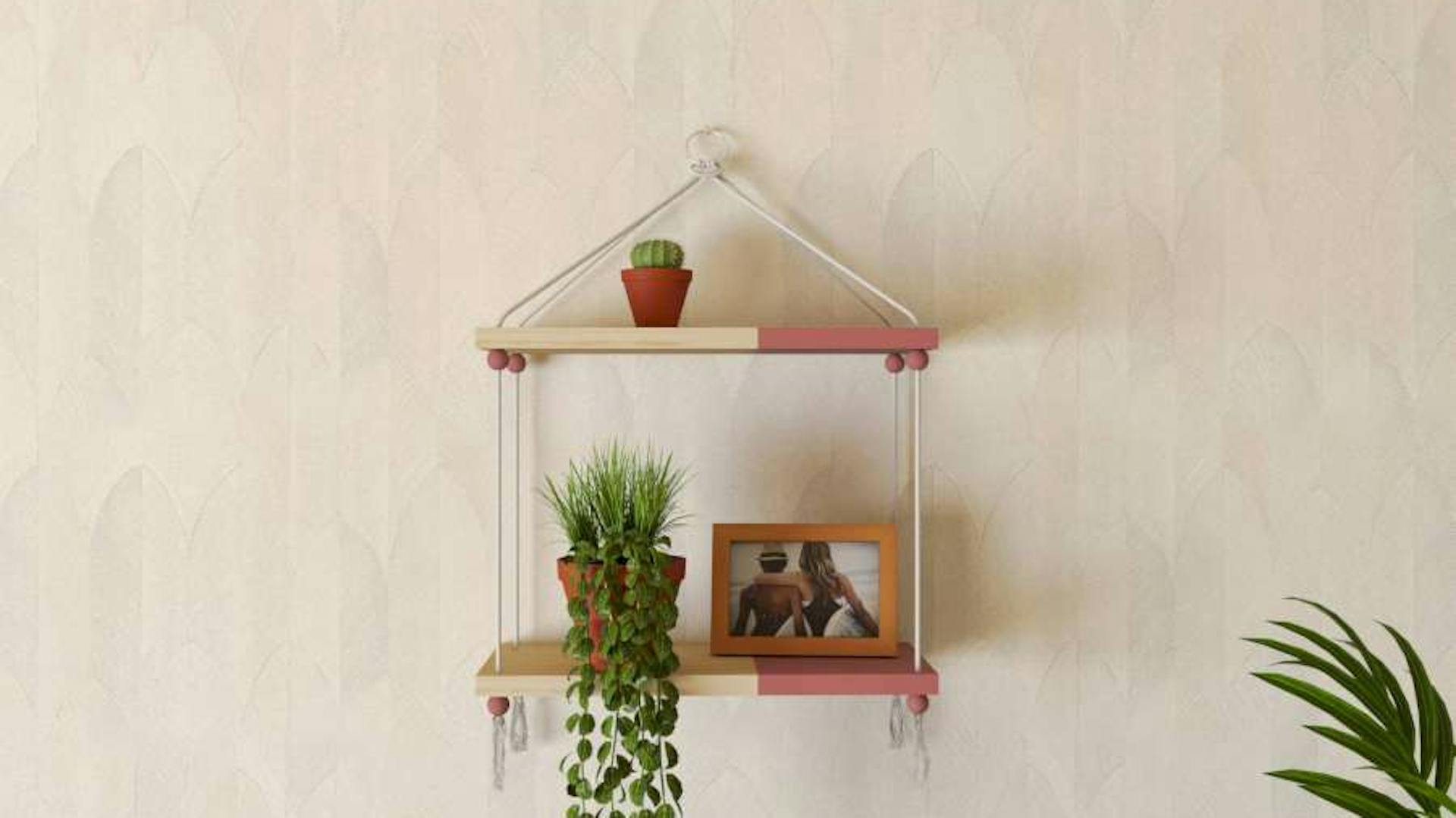 Das DIY-Hängeregal Seil ist an einer hellen Wand über einer Couch befestigt. Im Hängeregal sind Pflanzen und ein Foto platziert.