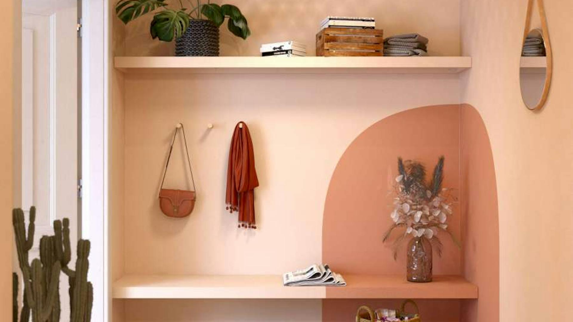 Ein Flur in warmem Beige und einer orangen Farbfläche in der Ecke, nutzt eine an der Wand angebrachten Holzplatte als Stauraum