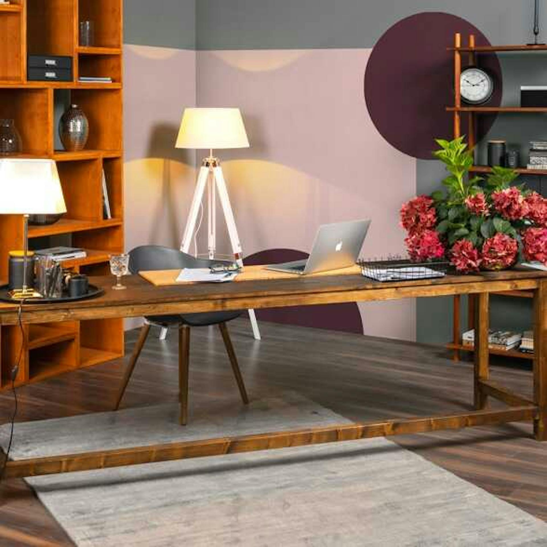 In einem Arbeitszimmer mit grauen Wänden und rosa-violetten Farbflächen steht Schreibtisch Egon mit einem Stuhl vor zwei Regalen und einer Lampe.