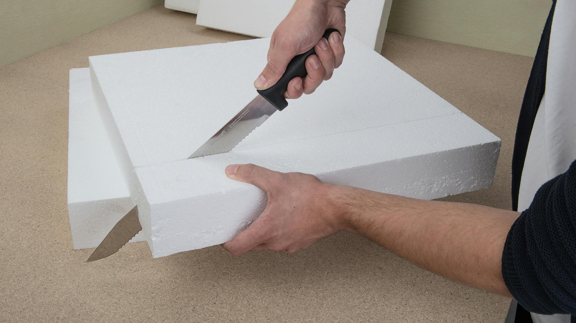 Hände schneiden Styropor mit Dämmstoffmesser