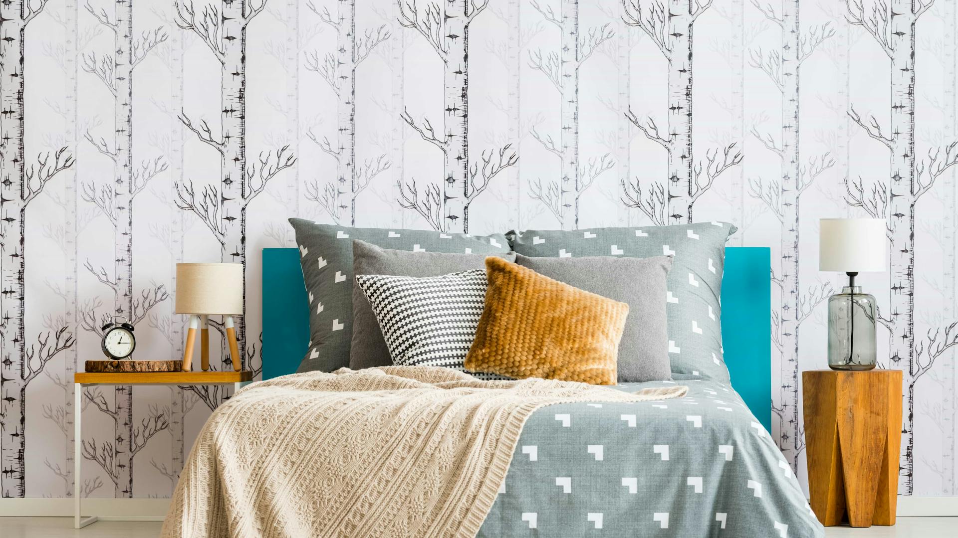 Gemütliches Bett mit Kissen und grauer Decke vor tapezierter Wand im Schlafzimmer