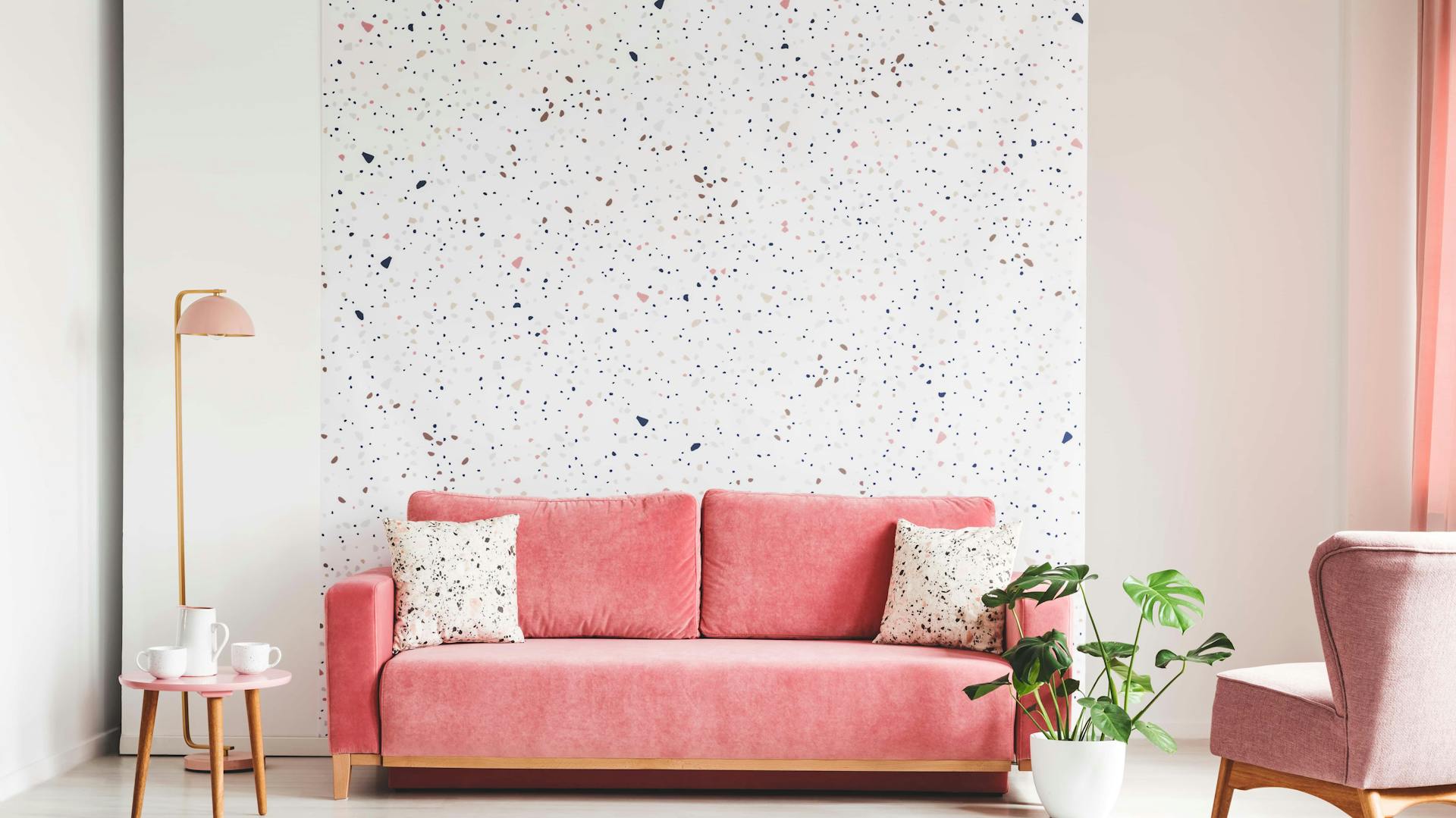 Wohnzimmer mit rosa Sofa, Sessel und Tapete mit rosa-weißem Muster