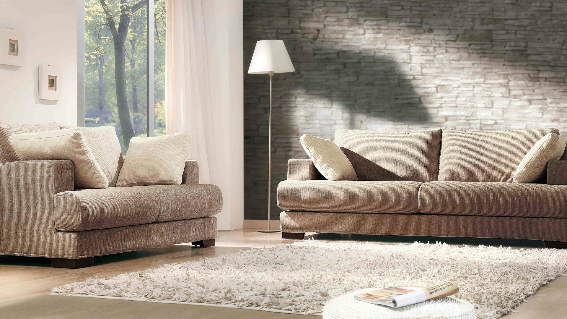 Tapete in Steinmauer-Optik in braun eingerichtetem Wohnzimmer mit Sofa, Sessel und Teppich