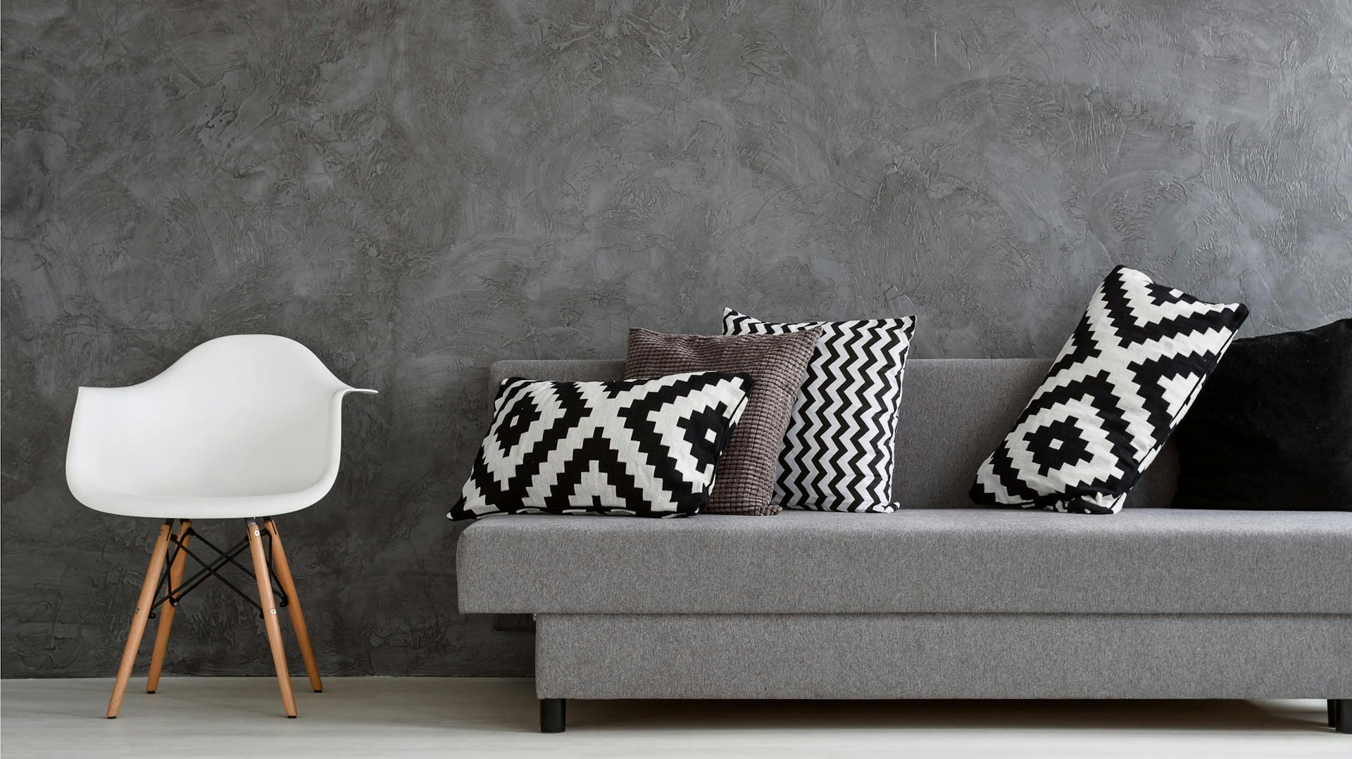 Tapete in grau-melierter Optik, davor ein graues Sofa und ein weißer Stuhl.
