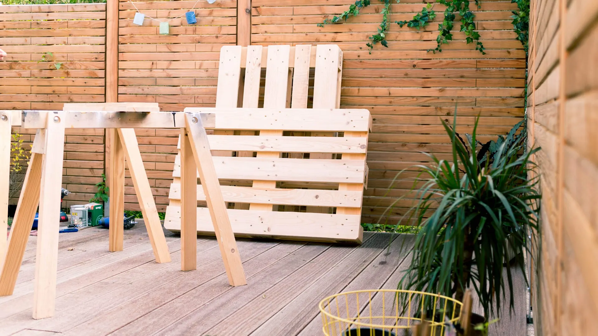 Paletten stehen bereit zur Verarbeitung an Sichtschutzzaun aus Holz auf Terrasse.