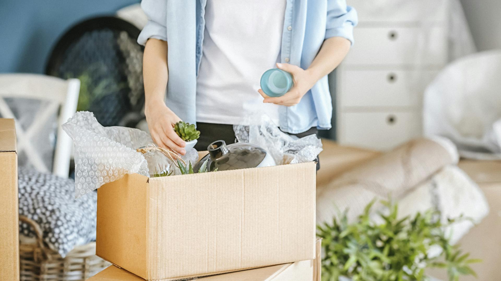 Mensch packt Dinge in Karton mit Luftpolsterfolie