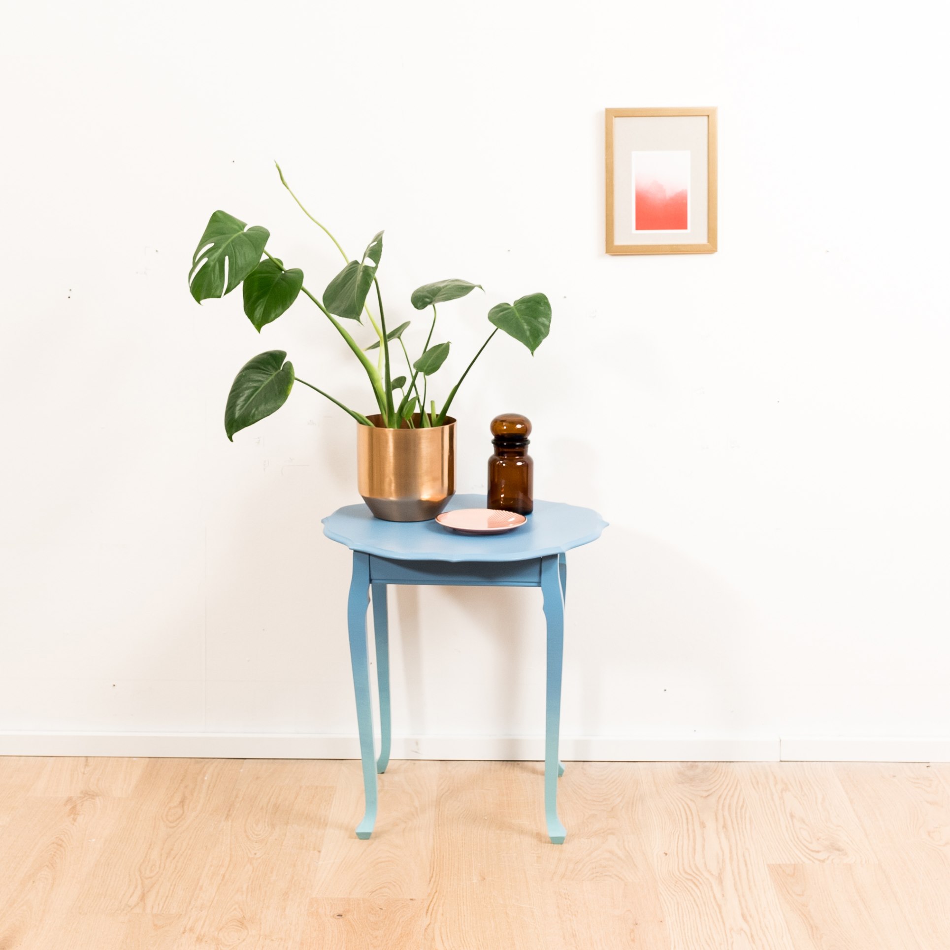 Tavolino da appoggio con sfumatura di colore da blu a celeste. Sopra si vedono una decorazione e una pianta da appartamento.