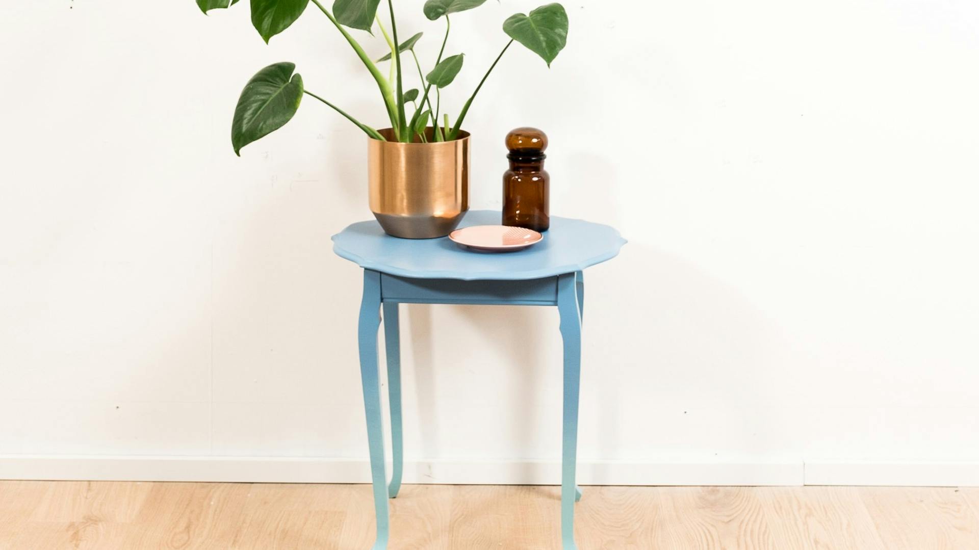 Tavolino da appoggio con sfumatura di colore da blu a celeste. Sopra si vedono una decorazione e una pianta da appartamento.