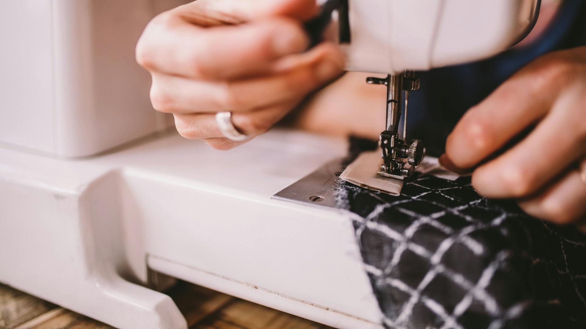 Detailní záběr šití: Žena zpracovává látku na šicím stroji.