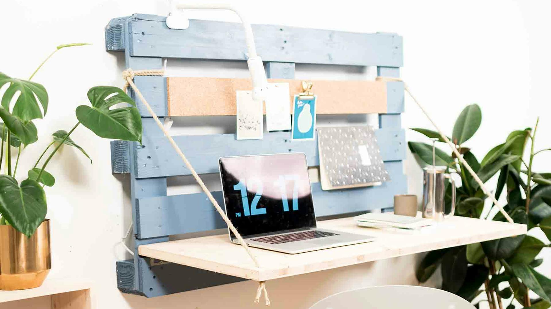 Na paletě připevněné ke zdi je pomocí provázku upevněna deska, která slouží jako sklopná deska stolu.