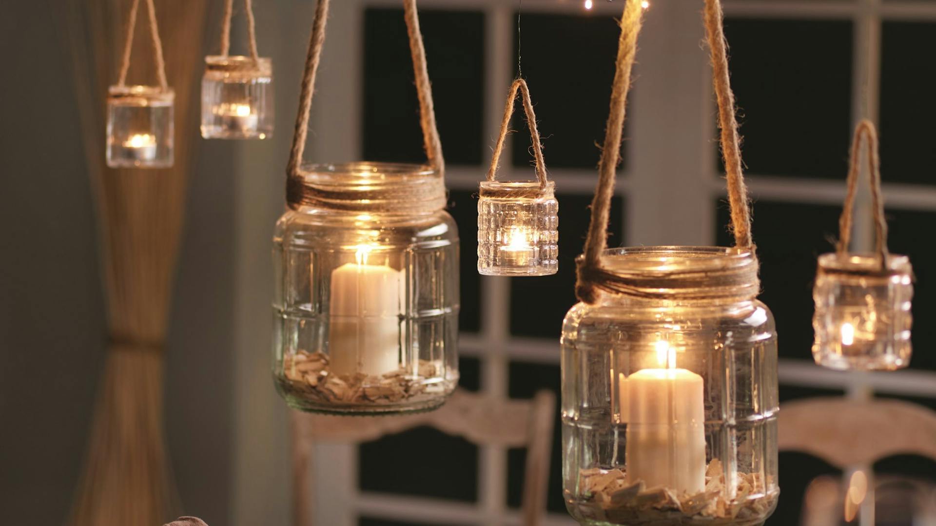 Lumini appesi a un’asta fissata al soffitto e vecchi vetri uniti con spago all’asta.