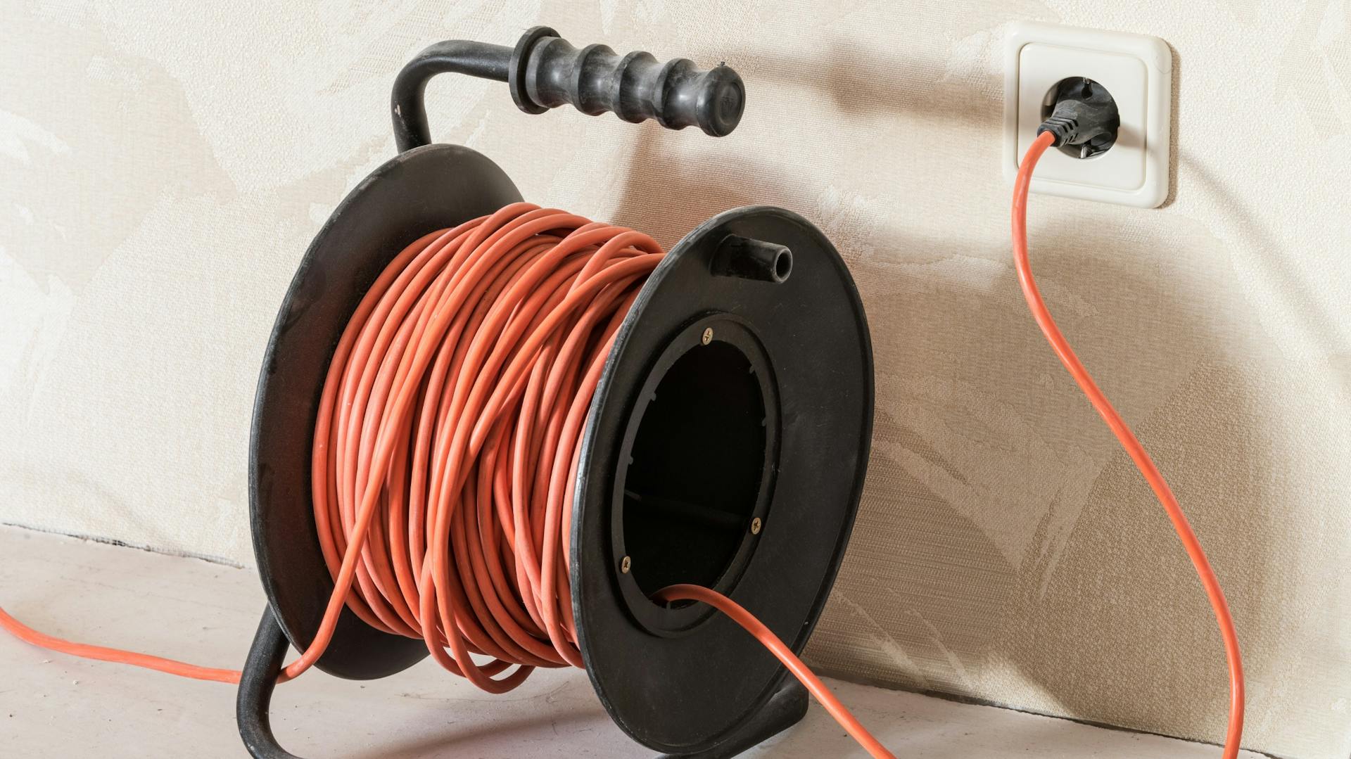Kabeltrommel mit orangefarbenem Kabel an Steckdose