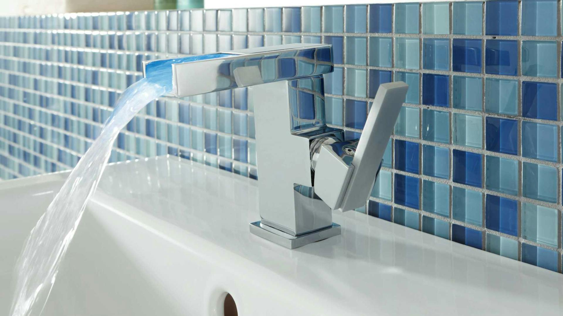 Hinter einem Wasserhahn wurden Glasfliesen im Mosaik-Muster angebracht.