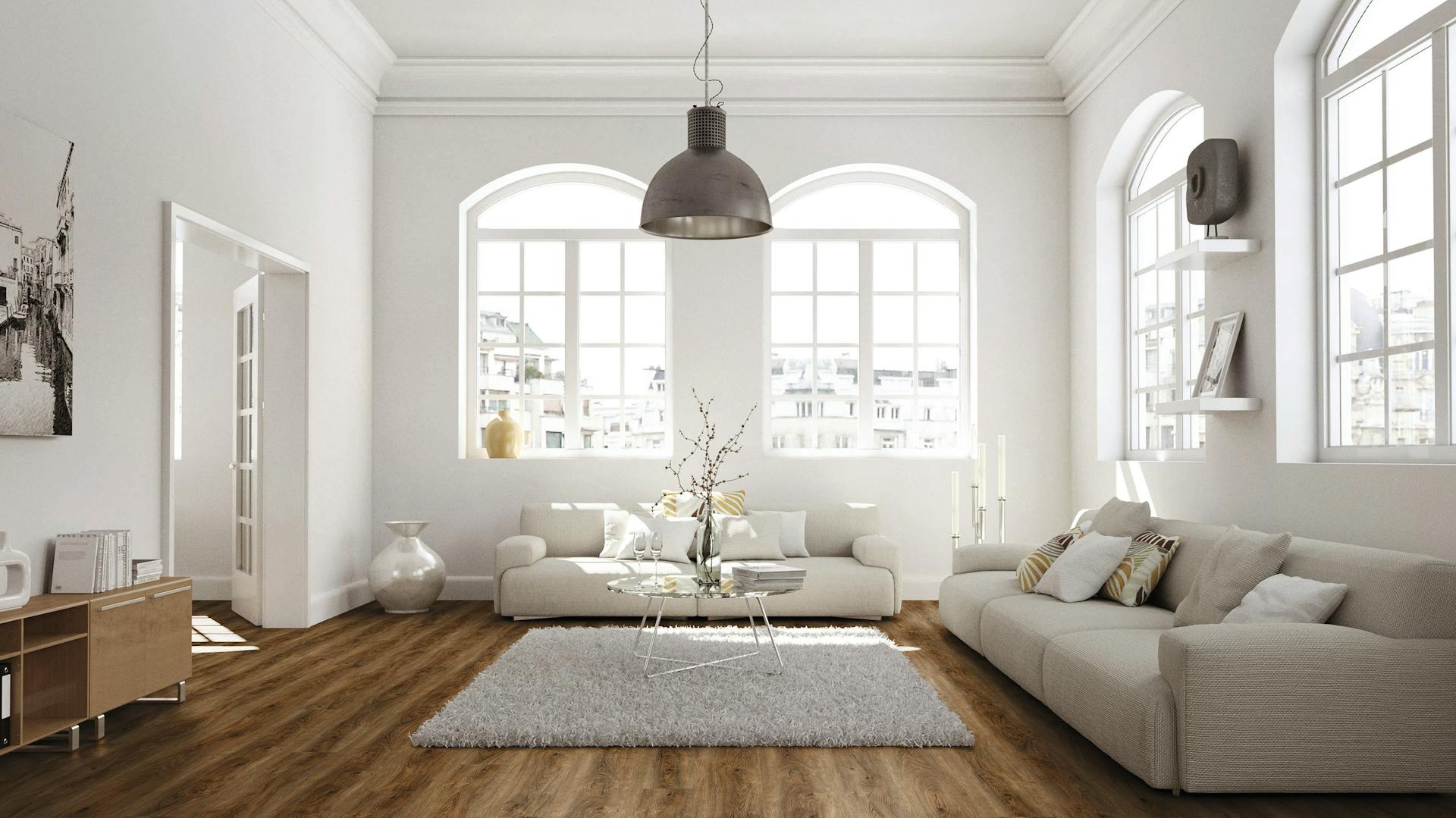 Ein Wohnzimmer mit Holzfußboden, großen Fenstern und weiß gestrichenen Wänden.