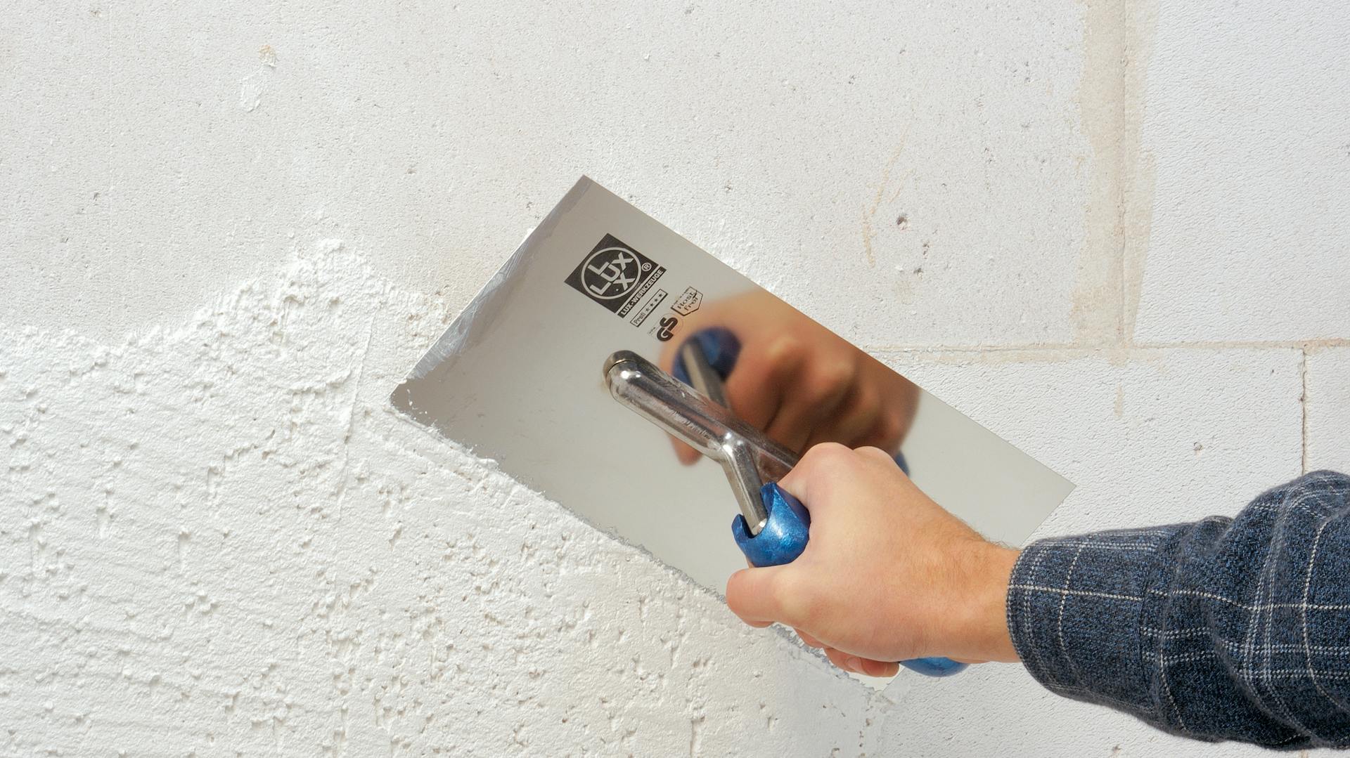Eine Wand wird vom Heimwerker mit einer Glättekelle verputzt.