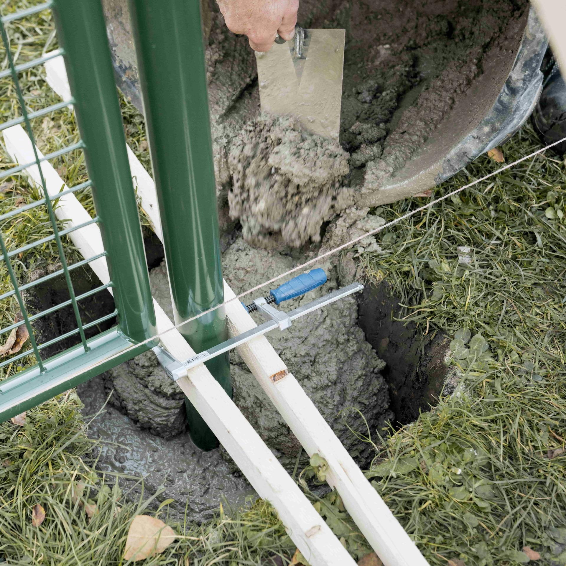 Heimwerker betoniert den Pfosten eines Gartentores ein.