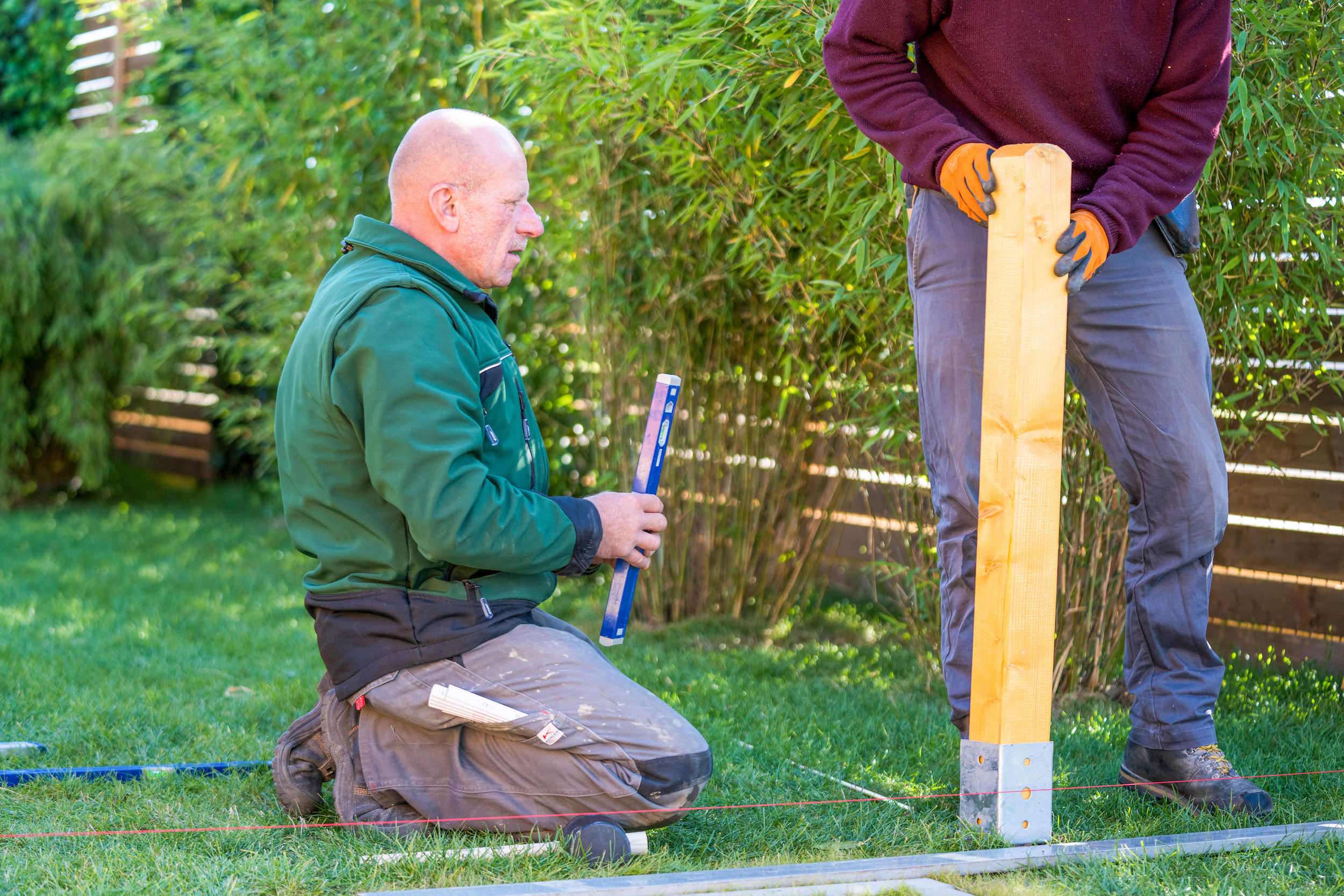 Mann hält einen Holzpfosten an eine Bodenhülse