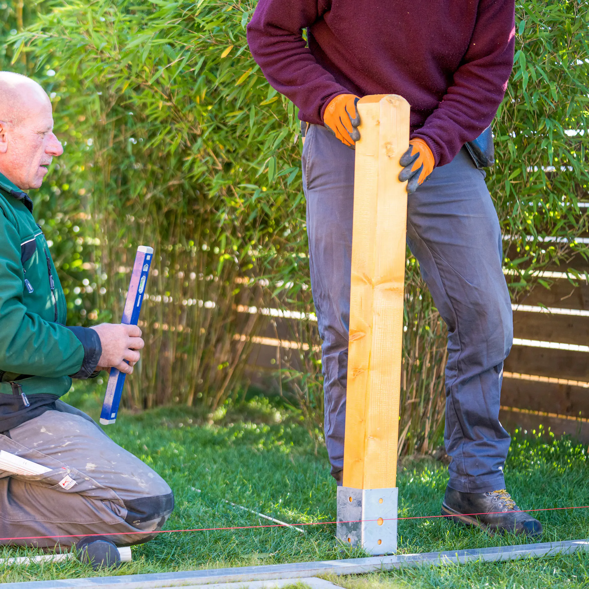 Mann hält einen Holzpfosten an eine Bodenhülse