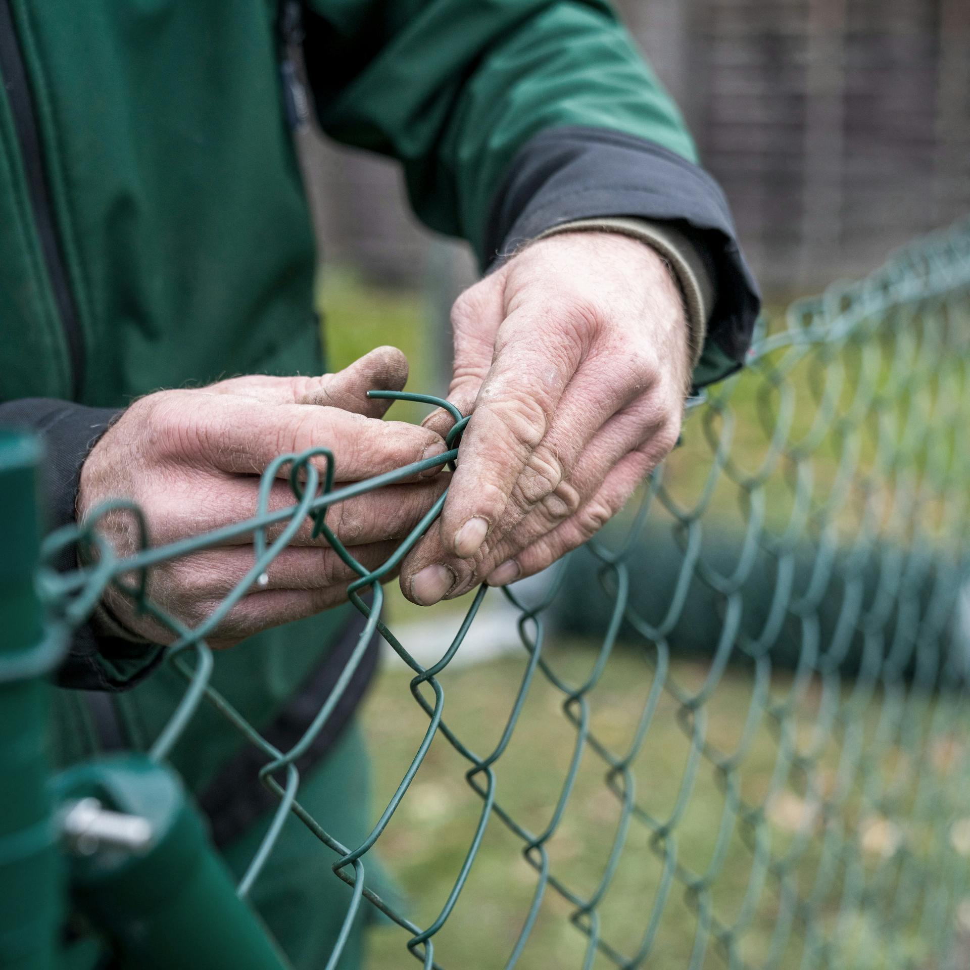Muž ohýba drôtené pletivo okolo napínacieho drôtu