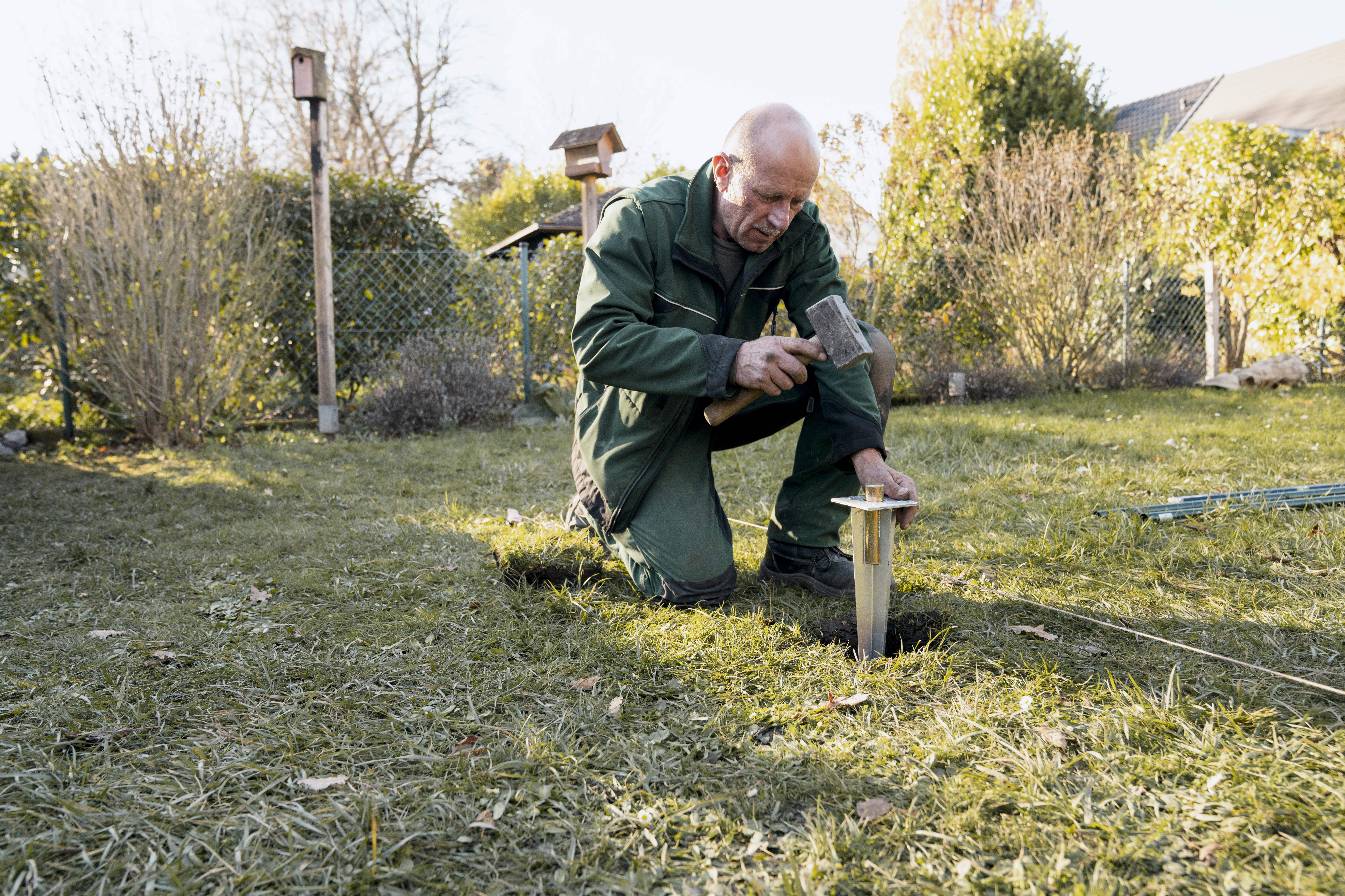 Záhradník zatĺka gumeným kladivom kotevnú pätku do zeme.