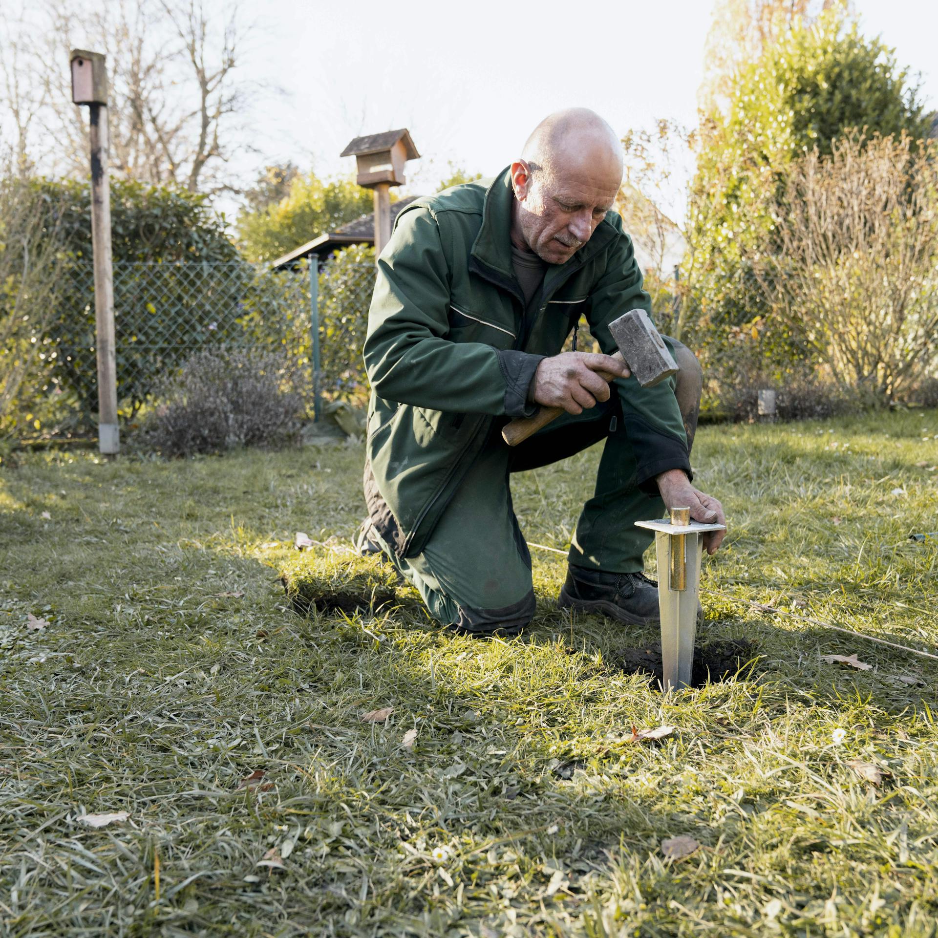 Záhradník zatĺka gumeným kladivom kotevnú pätku do zeme.